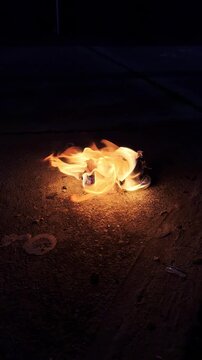 Peque&ntilde;a fogata ardiendo en el suelo por la noche, llamas parpadeantes, luz c&aacute;lida.