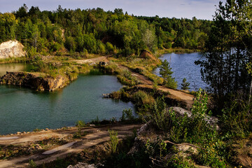 Obraz premium Scenic basalt quarry lake with steep stone walls, green forest, and reflections creating a peaceful natural landscape.