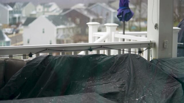 Snow covers houses in a cold winter day in a quiet neighborhood with limited visibility and gray skies. Snow falls on rooftops in a neighborhood and clouds block the sun, making it hard to see far awa