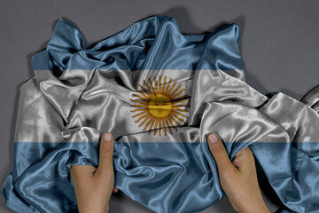 Argentina Flag Grasped by Hands Draped in Silk Across Grey Background