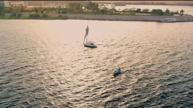 Aerial drone shot of traditional Egyptian felucca sailing on the Nile River at sunset in Aswan, Egypt