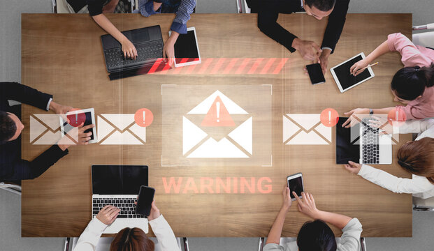 A diverse business team engages in a serious discussion about email security threats. Digital warning symbols highlight the need for awareness in a modern office setting. Gantry - Powered by Adobe