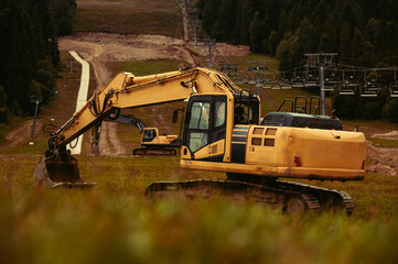 A large yellow hydraulic excavator parked on a grassy hillside. Undergoing construction or land modification. Preparing terrain for snowmaking infrastructure