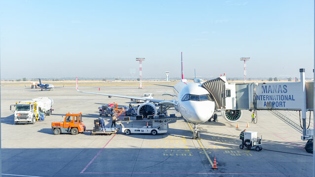 Airplane at Manas International Airport being serviced by ground crew, showcasing busy airport operations and aircraft maintenance activities