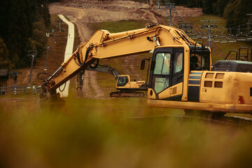 A large yellow hydraulic excavator parked on a grassy hillside. Undergoing construction or land modification. Preparing terrain for snowmaking infrastructure