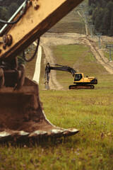 A large yellow hydraulic excavator parked on a grassy hillside. Undergoing construction or land modification. Preparing terrain for snowmaking infrastructure