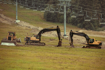 A large yellow hydraulic excavators parked and serviced on a grassy hillside. Undergoing construction or land modification. Preparing terrain for snowmaking infrastructure