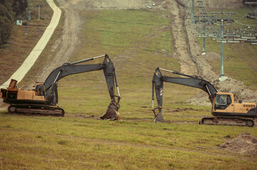 A large yellow hydraulic excavators parked and serviced on a grassy hillside. Undergoing construction or land modification. Preparing terrain for snowmaking infrastructure