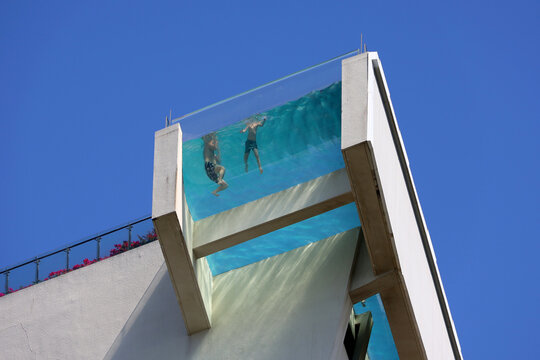 People in swimming pool with transparent glass bottom on a roof of hotel building