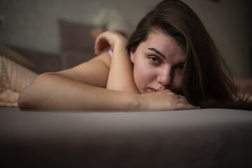 Obraz premium Young woman with long dark hair resting on a couch, wearing a white shirt, with soft pillows and a neutral background creating a cozy indoor atmosphere