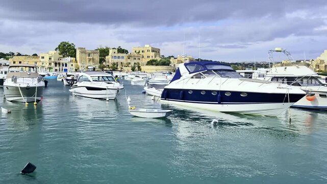 Birzebbuga, Malta &ndash; sleek motor yachts in calm harbor water with traditional architecture in the background