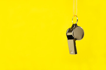 A metal whistle with bright yellow lanyard hanging isolated against yellow background with copy...