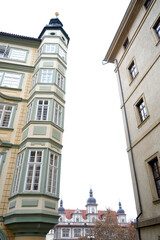 Obraz premium Narrow street view between historic buildings with tall ornate facade and tower detail, upward perspective showing classic architecture and quiet urban atmosphere.