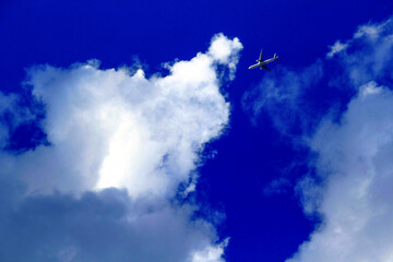 An airplane soaring through a bright blue sky amidst fluffy white clouds