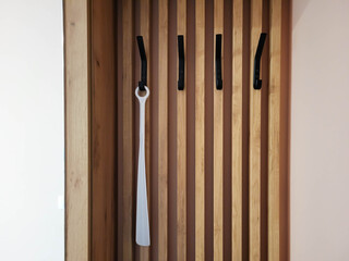 In the hallway, there is a wooden wall hanger with black hooks and a white shoe horn.