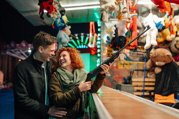 Fototapeta premium Happy couple enjoying fairground shooting game at night