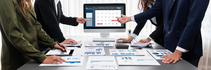 Panorama shot analyst team utilizing BI Fintech to analyze financial report with laptop. Businesspeople analyzing BI data dashboard displayed on laptop screen for business insight. Prodigy