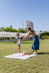 Mother and daughter enjoying an outdoor picnic in an urban park on a sunny day, the child running to her mom for an embrace