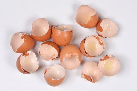 A top view of several empty cracked brown eggshells scattered on a plain white surface after cooking or baking