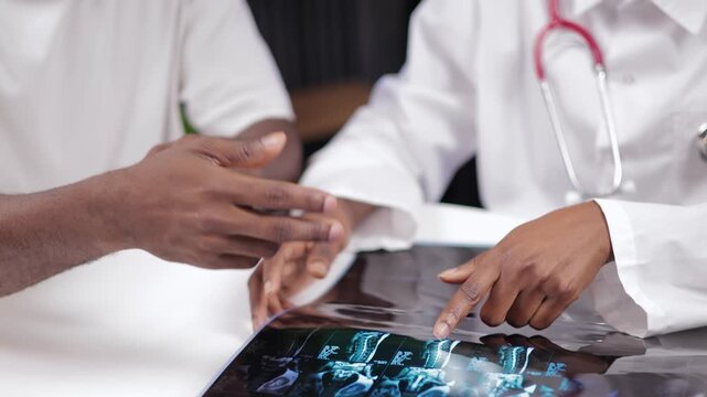 Consultation traumatologist African doctor discussing MRI scan x-rays with male patient in medical clinic office, Help with back injuries, hernias and spinal protrusions.