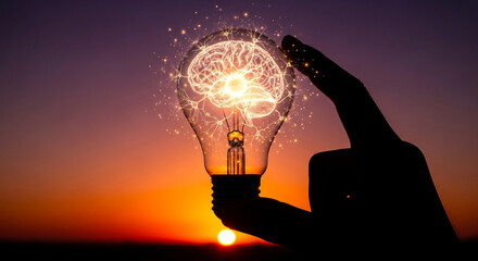 Silhouette hand holds illuminated lightbulb showing brain, sunset background, symbolizes idea, innovation, intelligence, knowledge, creativity