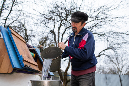 Grandpa draws water from a well and pours it into a bucket. Countryside