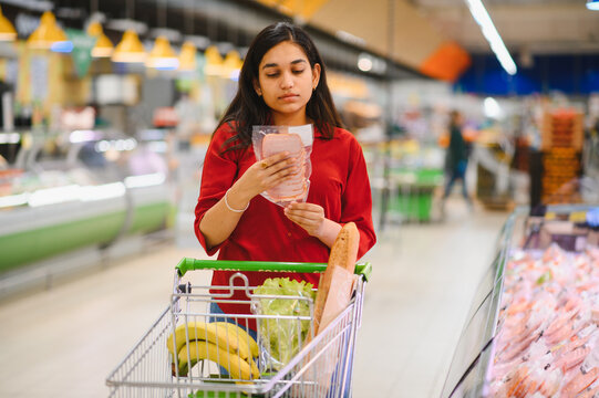 Woman shopping for groceries choosing packaged meat at supermarket