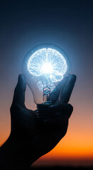 Hand holding lightbulb with glowing brain inside, sunset background.  Symbolizes intelligence, idea, innovation, knowledge