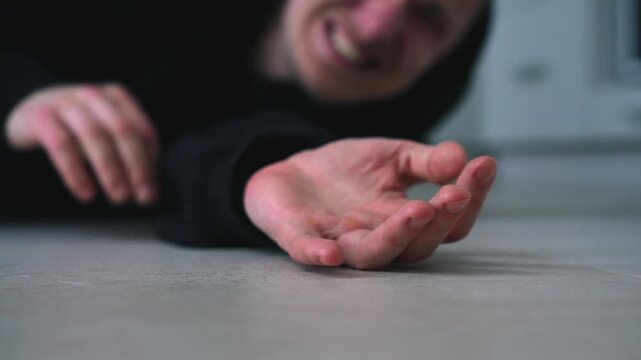 A man stretches his arm while lying on the floor.
The man falls to the floor and injures himself.
The man calls for help.