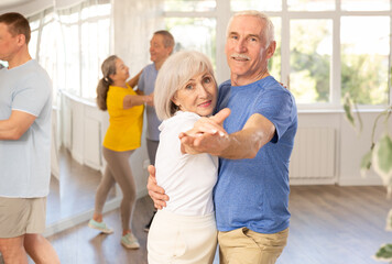 Positive active elderly couple enjoying slow foxtrot in dance studio. Amateur social dancing concept