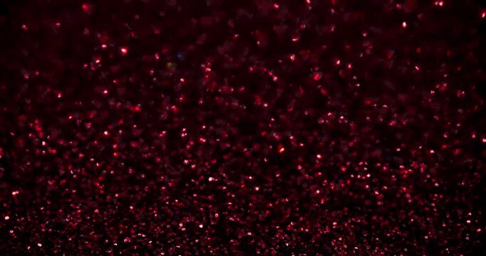Red heart glitter sparkles on a dark backdrop with soft diagonal shadow bands, created in stop-motion style. Romantic abstract texture for Valentine&rsquo;s Day, overlays, and looping backgrounds.