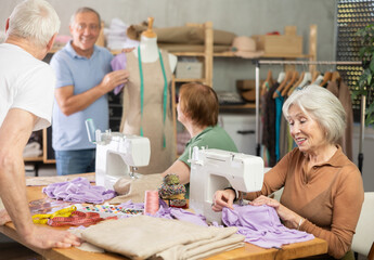 Obraz premium Elderly male teacher shows group of elderly people how to sew clothes on mannequin at master class