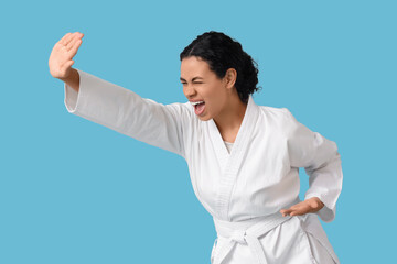 Young African-American woman with white belt practicing karate on blue background © Pixel-Shot