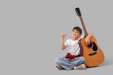 Cute boy with guitar pointing at something on light background