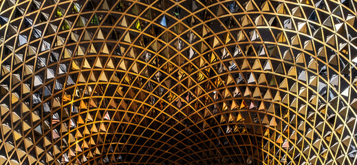 a modern architectural structure with a complex, curved design made of gold-tone metal and mirrored...