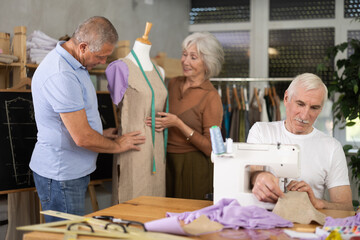 Obraz premium Group of elderly men and women sewing on machine and working with mannequin during master class