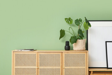 Obraz premium Wooden chest of drawers with houseplant and magazines near frames in living room