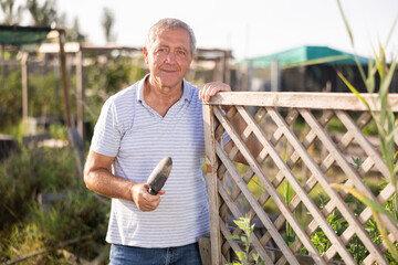 Portrait of happy elderly man with a hoe in her hands in her garden