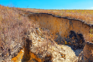 Deep gully cuts through eroded land, exposing layered soil with sparse vegetation clinging to surface. Degradation and the vulnerability of barren terrain to environmental forces