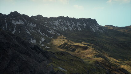Obraz premium sunlit alpine ridge at sunrise revealing vast rocky slopes and scattered snow patches under cool morning light, cinematic atmosphere with soft shadows