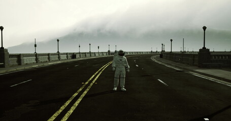 A solitary figure wearing an astronaut suit stands in the middle of a deserted road. The fog envelops the area, creating an eerie atmosphere at early dawn with dim lighting. © icetray