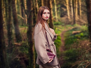 Portrait of a stunning young attractive woman wearing stylish jacket, blur forest park background....