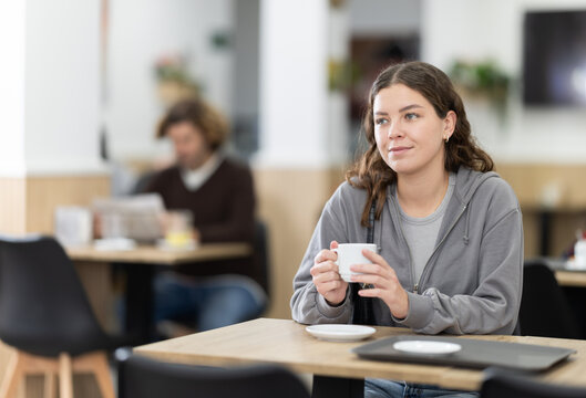 Attractive young female sitting alone at table in cozy cafe, drinking fragrant coffee