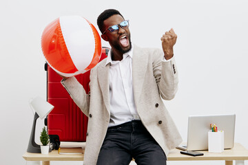 Excited cheerful young African-American man in smart casual clothing celebrating with a large beach ball in modern office environment, holding fist up in triumph, smiling, positive mood, lifestyle