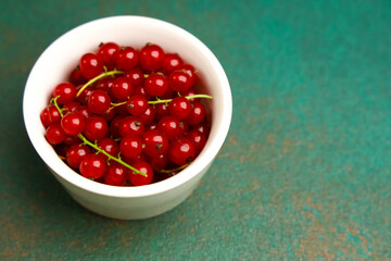 Fresh red currants in a white bowl on a green surface ready for cooking or snacking