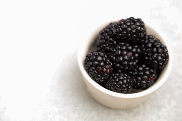 Fresh blackberries in a small bowl on a light surface during daylight