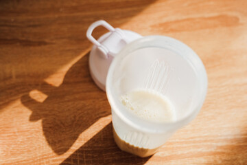 Cup with protein supplement for athletes in a shaker on a wooden surface at home during daytime