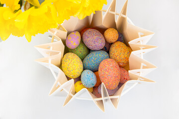 Colorful eggs in a basket surrounded by yellow flowers during spring celebration Easter