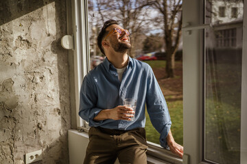 Obraz premium Young man enjoying morning sunlight by window with water