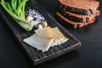 Pork fatback on a wooden cutting board with slices of rye bread, garlic,